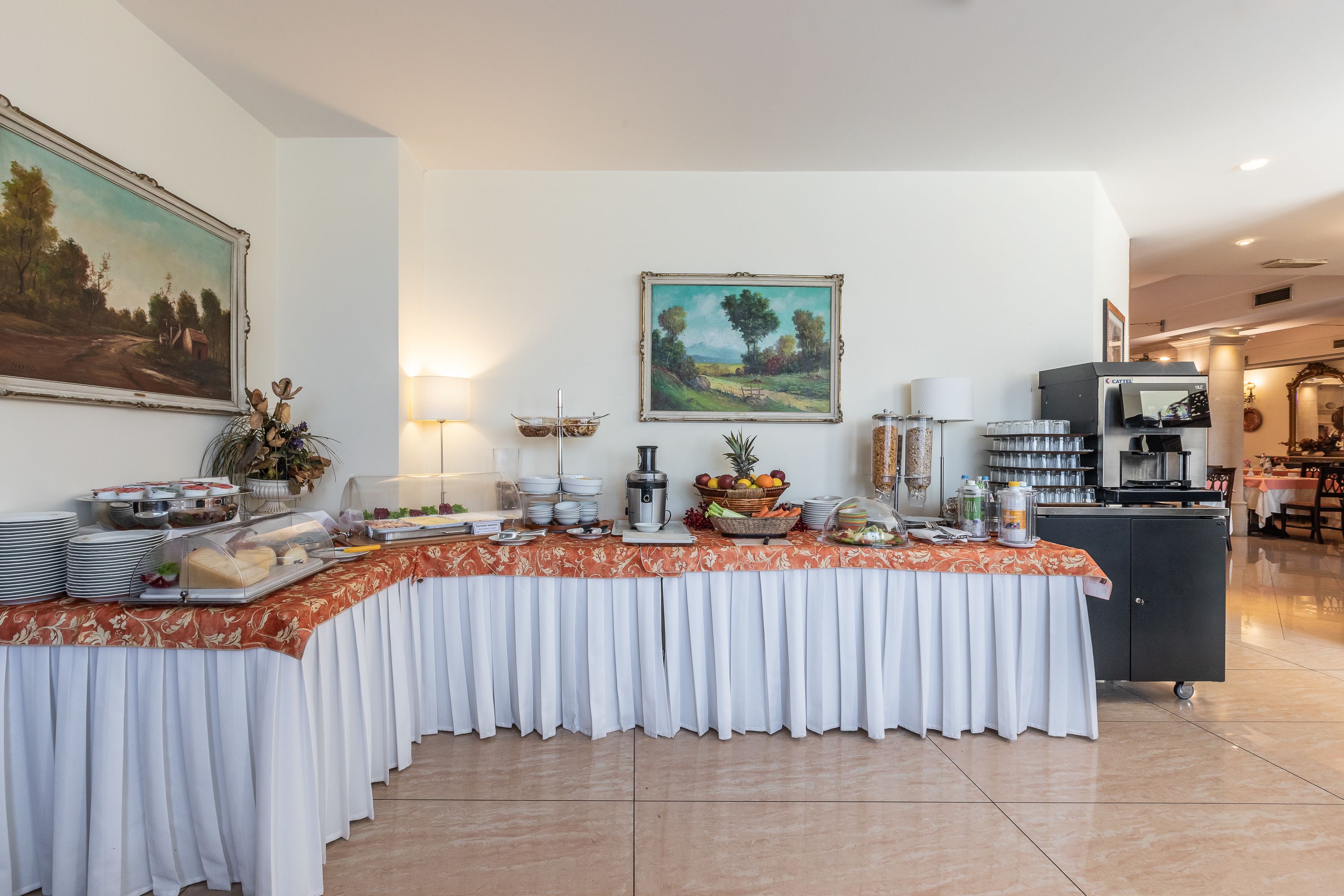 A buffet setup with various food items and a coffee station in a well-lit room with paintings on the walls.