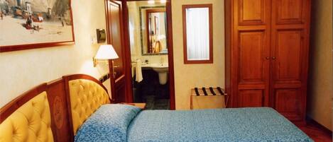 Habitación de hotel con dos camas, un armario de madera, un baño visible a través de una puerta abierta y un cuadro en la pared.