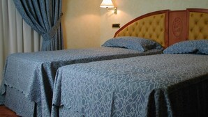 Een hotelkamer met twee bedden, een nachtkastje, een lamp en een raam met gordijnen.