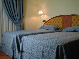 A hotel room with two beds, a nightstand, a lamp, and a window with curtains.