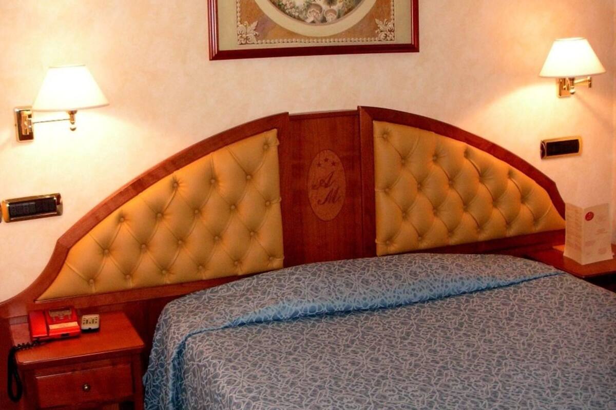 A hotel room with a large bed, a nightstand, a lamp, and a framed picture on the wall.