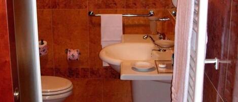 Un baño con inodoro, lavamanos y bañera. Hay toallas colgadas en un perchero.