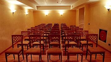 Una sala conferenze con file di sedie e tavoli di legno, applique a parete e un quadro incorniciato.