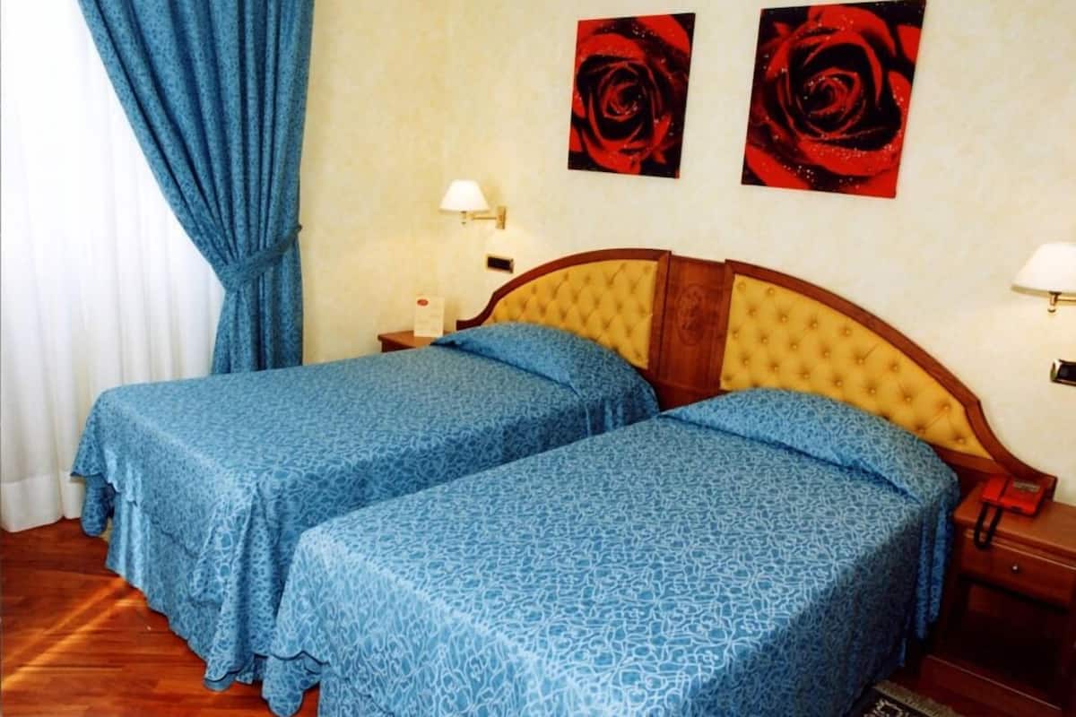 A room with two beds, a wooden headboard, a nightstand with a lamp, and two red rose paintings on the wall.