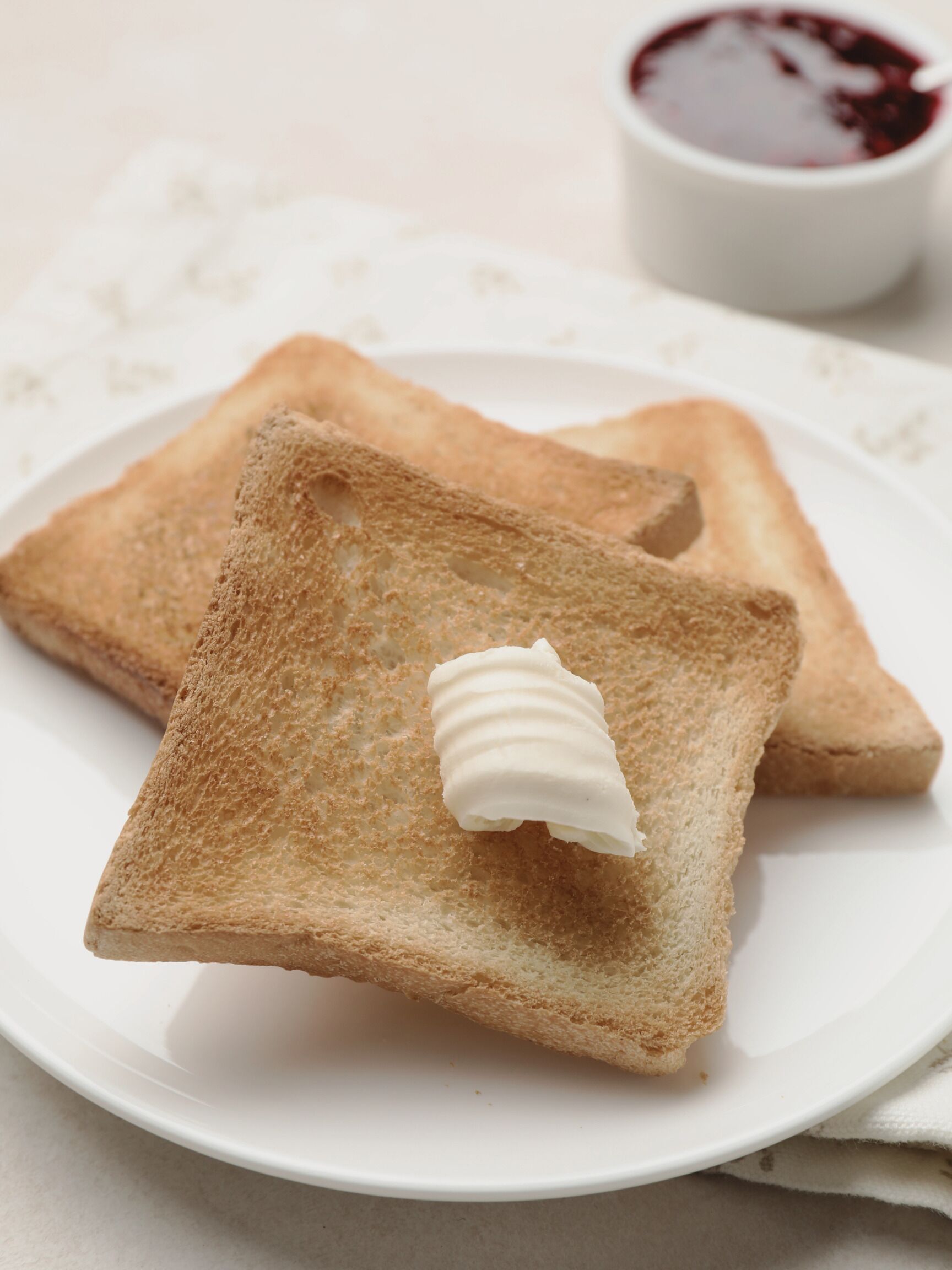 Two slices of toast with butter on a white plate, accompanied by a small bowl of jam.