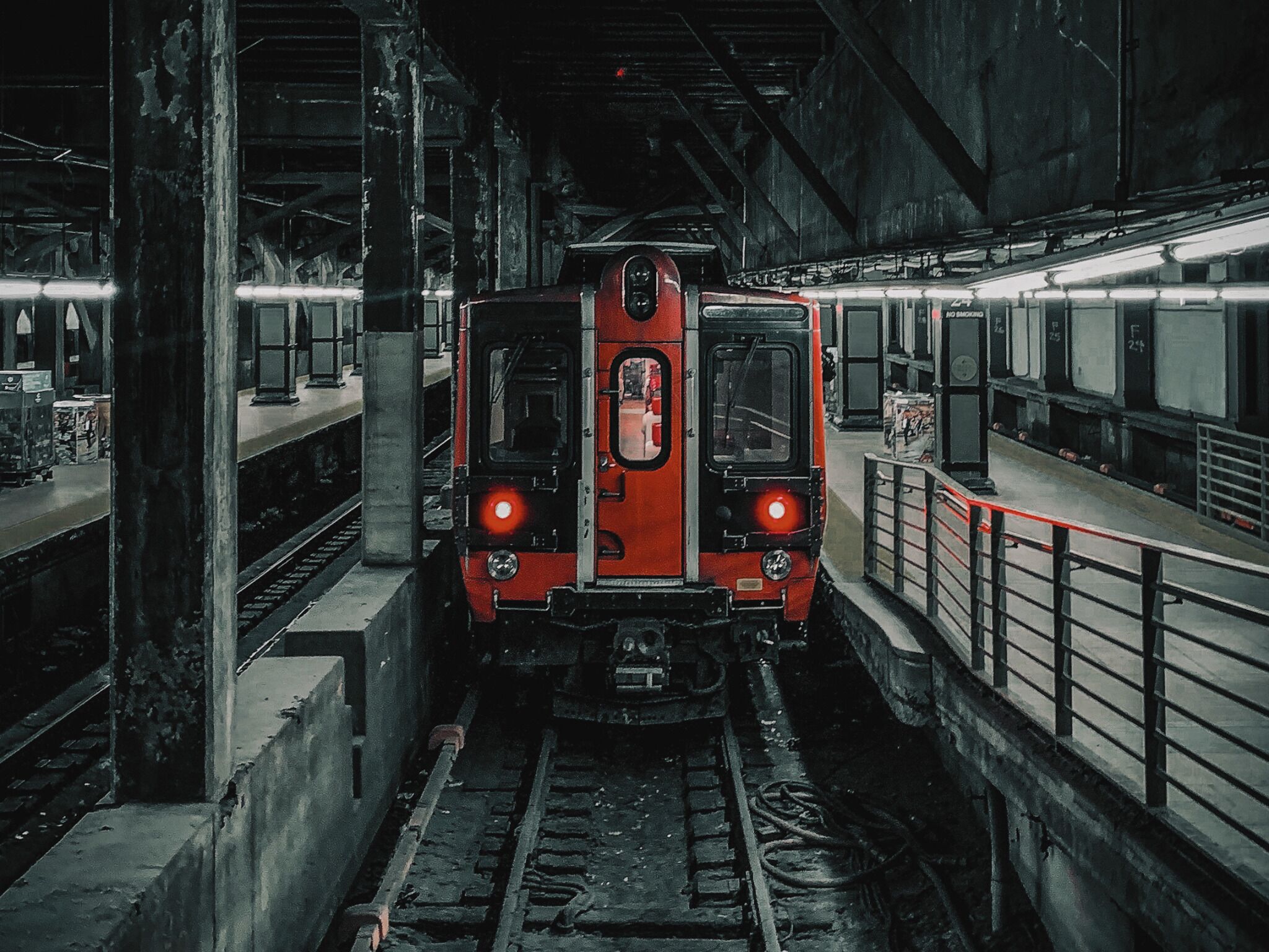 Een trein op een perron, met bovenliggende verlichting en een metalen hekwerk.