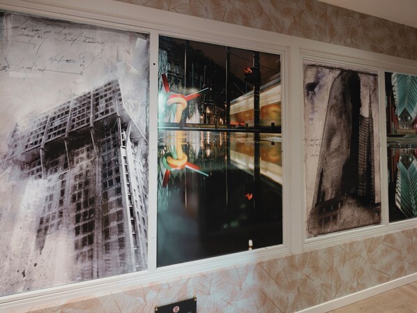 A wall with multiple framed artworks, including a building, a colorful abstract piece, and a detailed architectural drawing. - Kleos Hotel Milano by Kleos Group Collection (Milan)