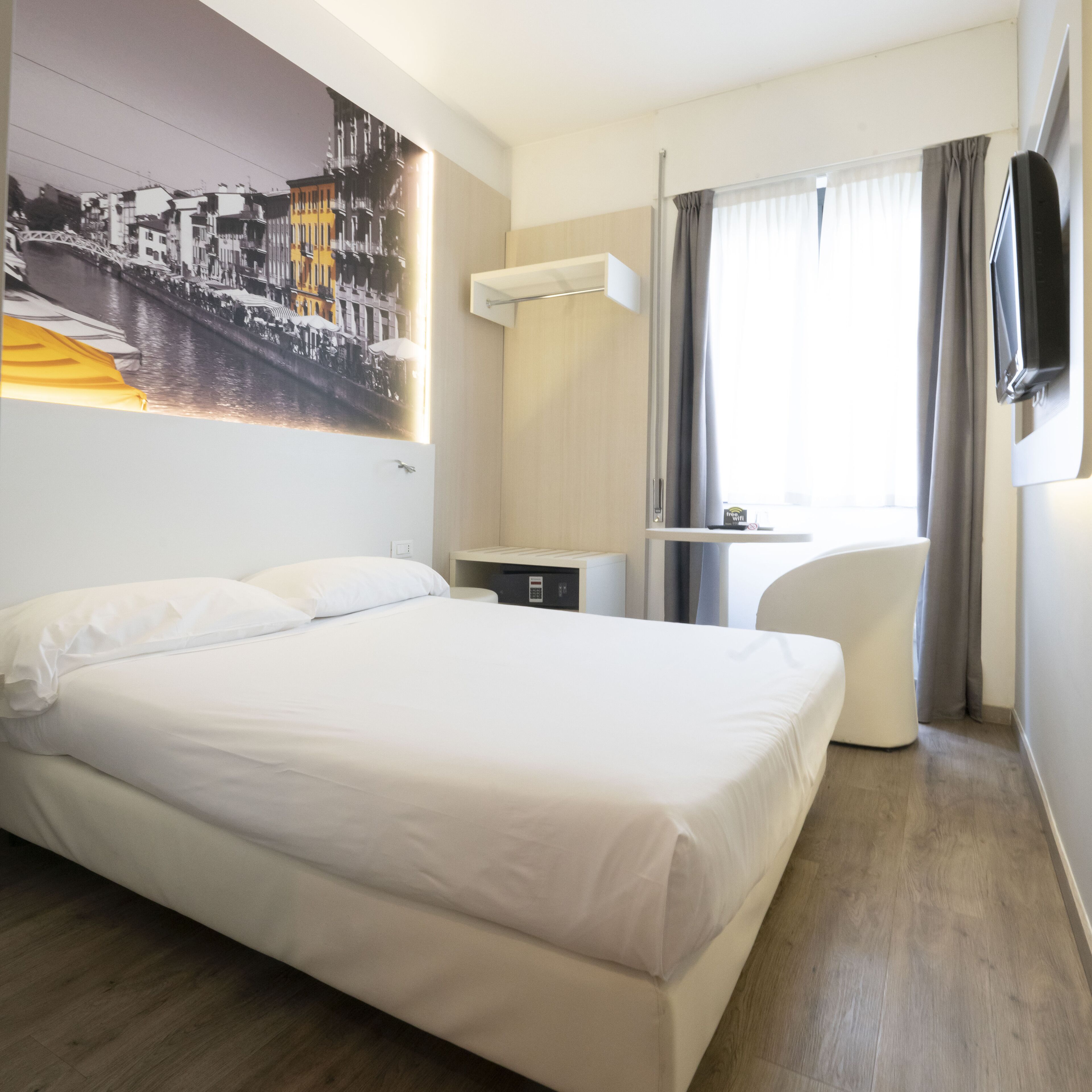 A hotel room with a large bed, a desk, a chair, and a TV.