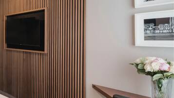 A modern room with a TV mounted on a wooden panel wall, a framed black and white photo, and a vase with flowers.