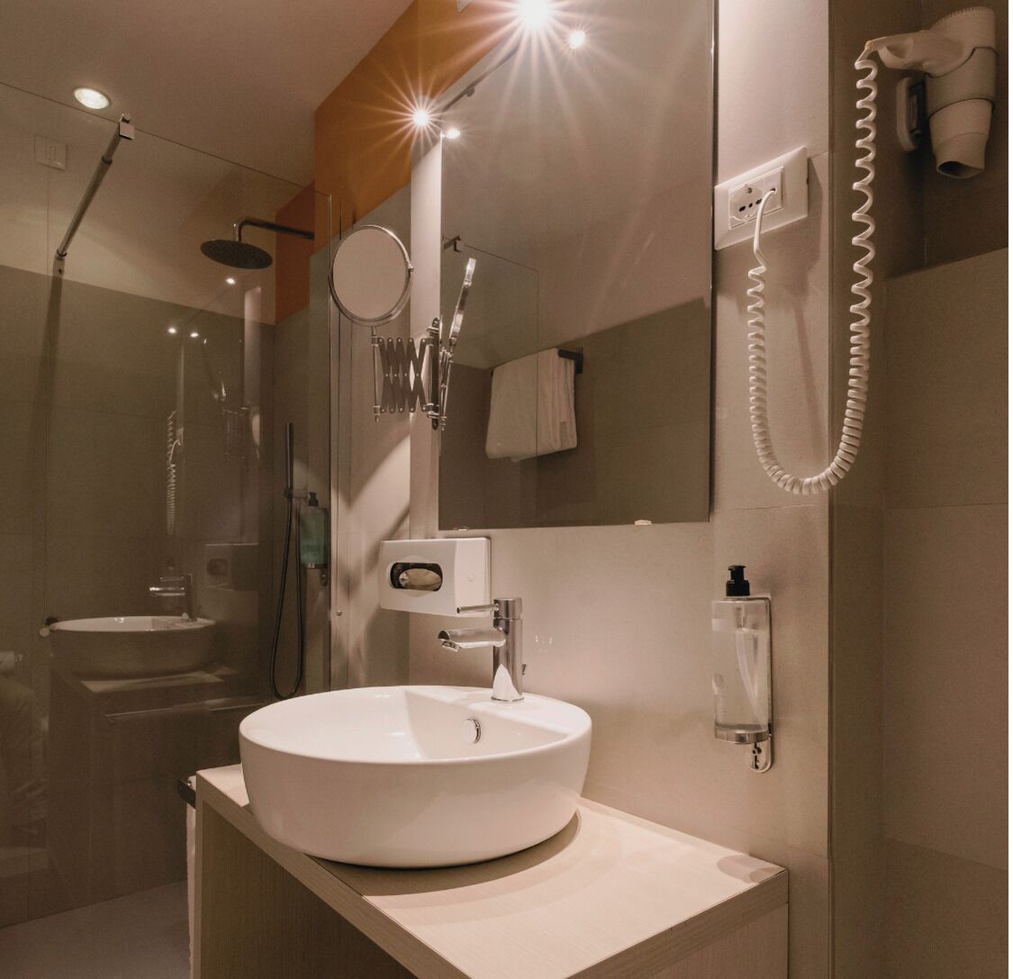 Un baño moderno con un lavabo redondo, un cabezal de ducha de mano, un perchero y un secador de pelo fijado a la pared.