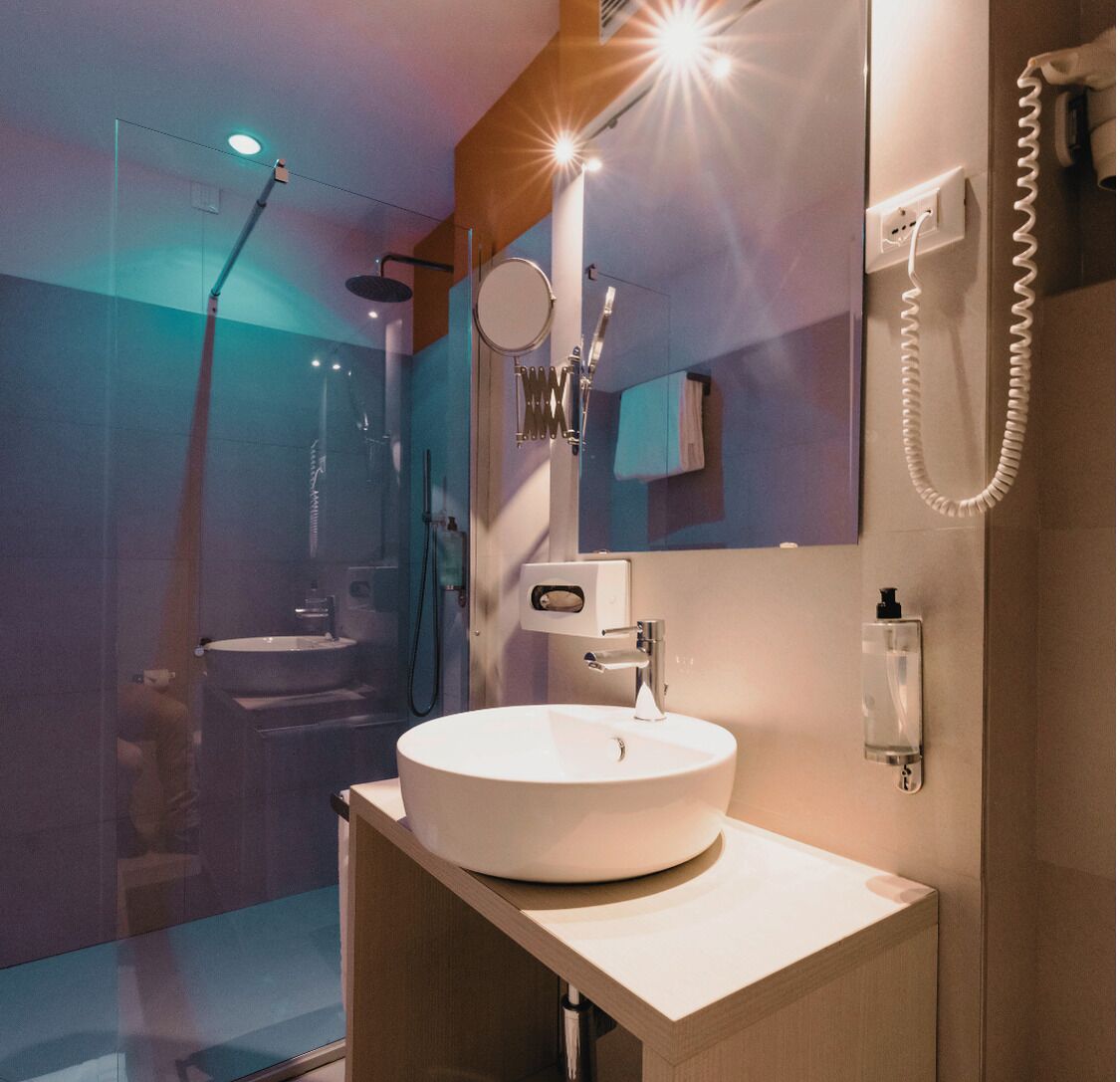 A modern bathroom with a round sink, a mirror, a handheld showerhead, and a glass-enclosed shower area.