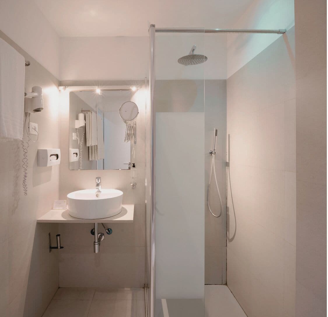 Un baño moderno con ducha de vidrio, espejo redondo y lavamanos blanco.