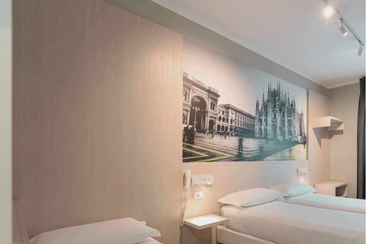 A hotel room with two beds, a wall-mounted phone, and a painting of a cityscape.
