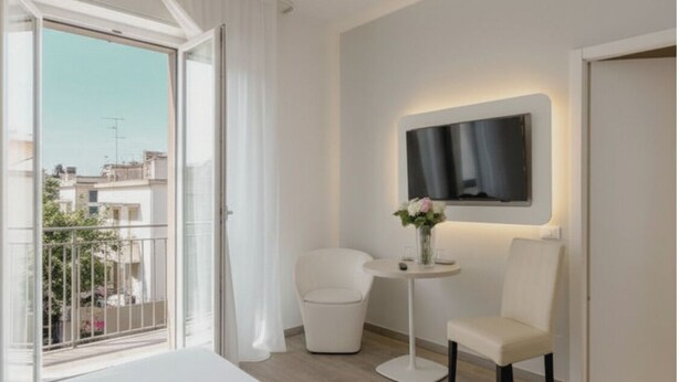 A modern hotel room with a large bed, a small round table with a vase, a chair, and a TV mounted on the wall. - Kleos Hotel Milano by Kleos Group Collection (Milan)