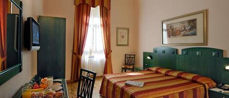 A hotel room with a bed, a desk with a computer, a chair, a window with curtains, and a painting on the wall.