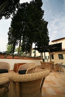 Muebles de mimbre dispuestos en un patio con un árbol grande y un edificio al fondo.
