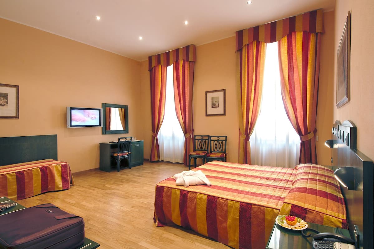 Ein Hotelzimmer mit zwei Betten, einem Schreibtisch, einem Sessel, einem Fernseher und einem Telefon.
