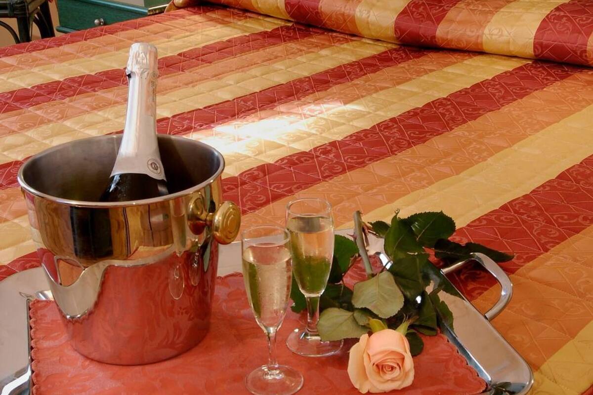 Ein Bett mit einem Metallkübel, der eine Flasche, ein Glas Wasser und ein Glas Champagner, eine Rose und ein Tablett auf einer Bettdecke enthält.