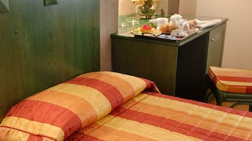 A hotel room with a bed, a desk with a vase of flowers, and a telephone on the nightstand.