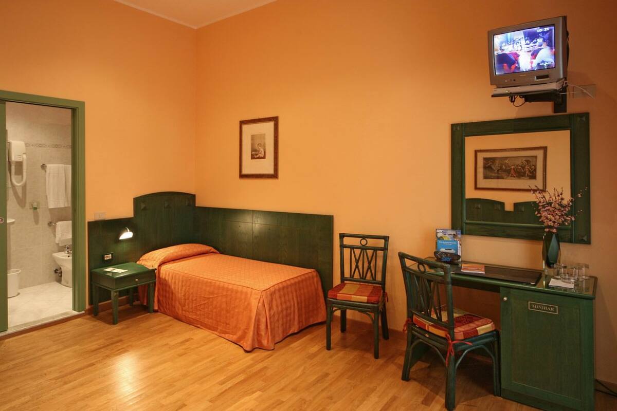 Ein Hotelzimmer mit Bett, Schreibtisch mit Stuhl, Fernseher und einem durch eine offene Tür einsehbaren Badezimmer.