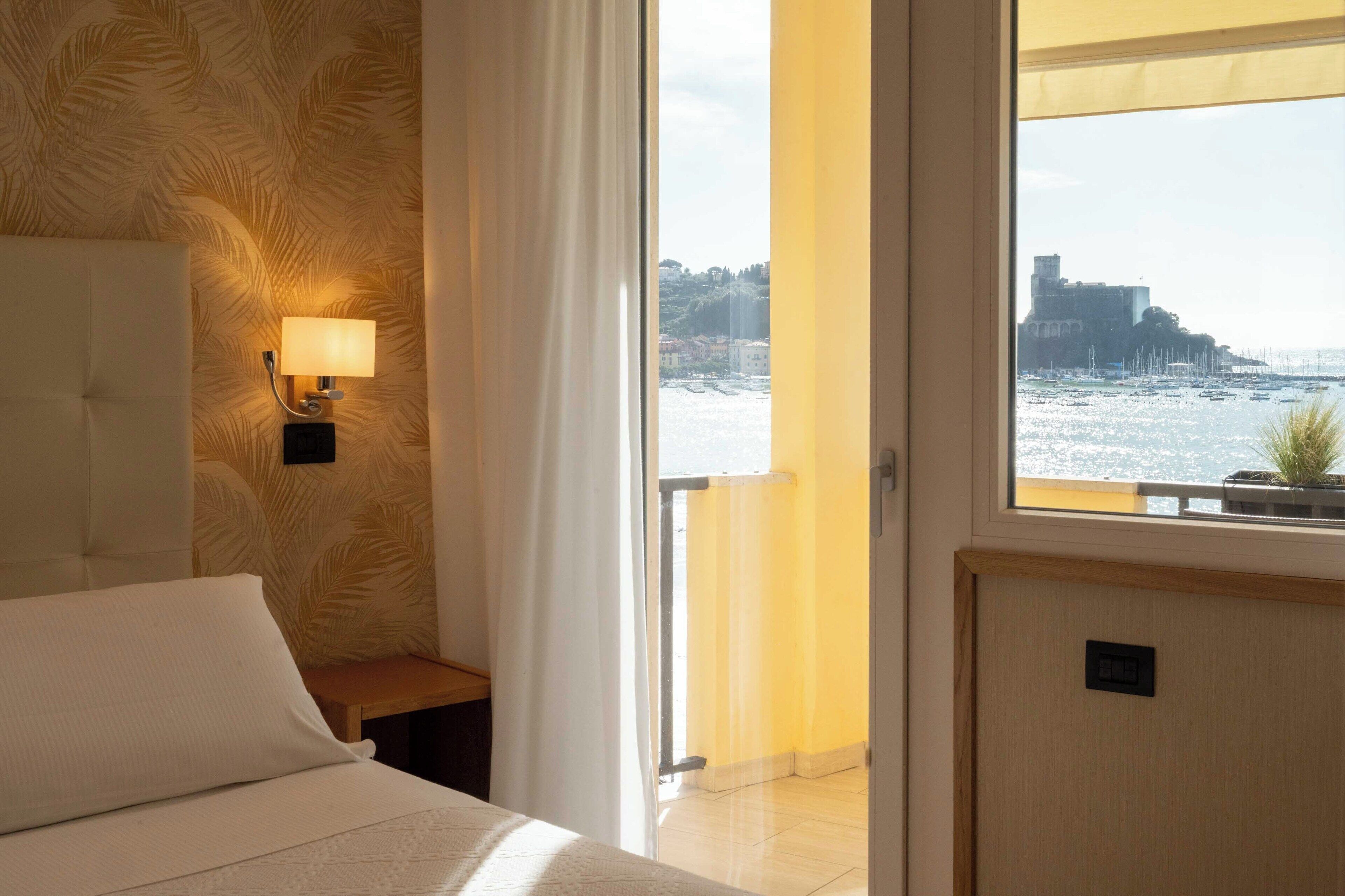 Une chambre d’hôtel avec un lit, une table de chevet, une lampe et une vue sur la mer et un château.