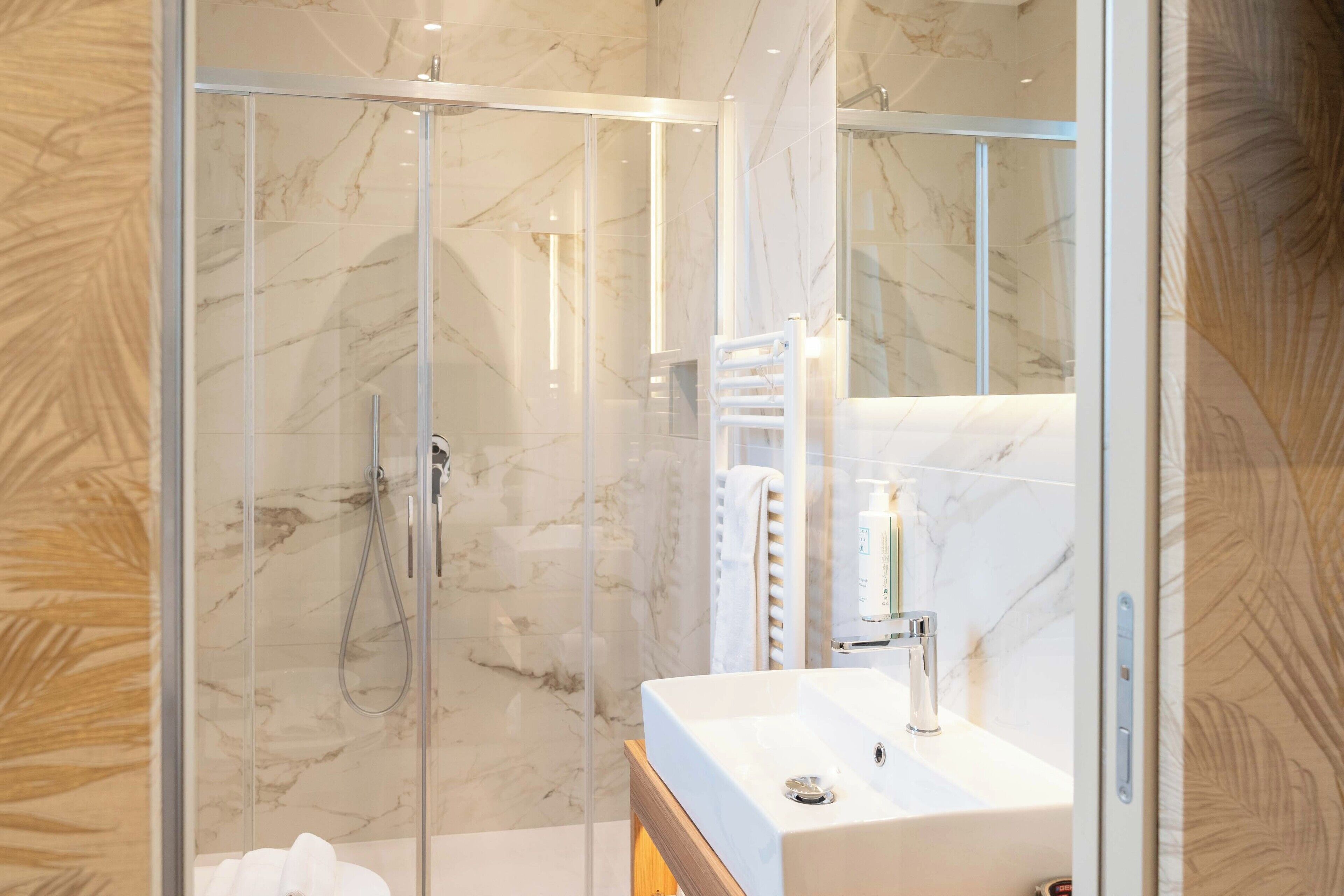 A modern bathroom with a glass-enclosed shower, a white sink, and a marble-tiled wall.