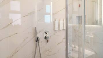 Un baño moderno con paredes de mármol, cabina de ducha de vidrio y artículos de aseo en un estante.