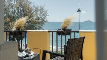 A balcony with wicker chairs, a table, and a view of the sea and distant island.
