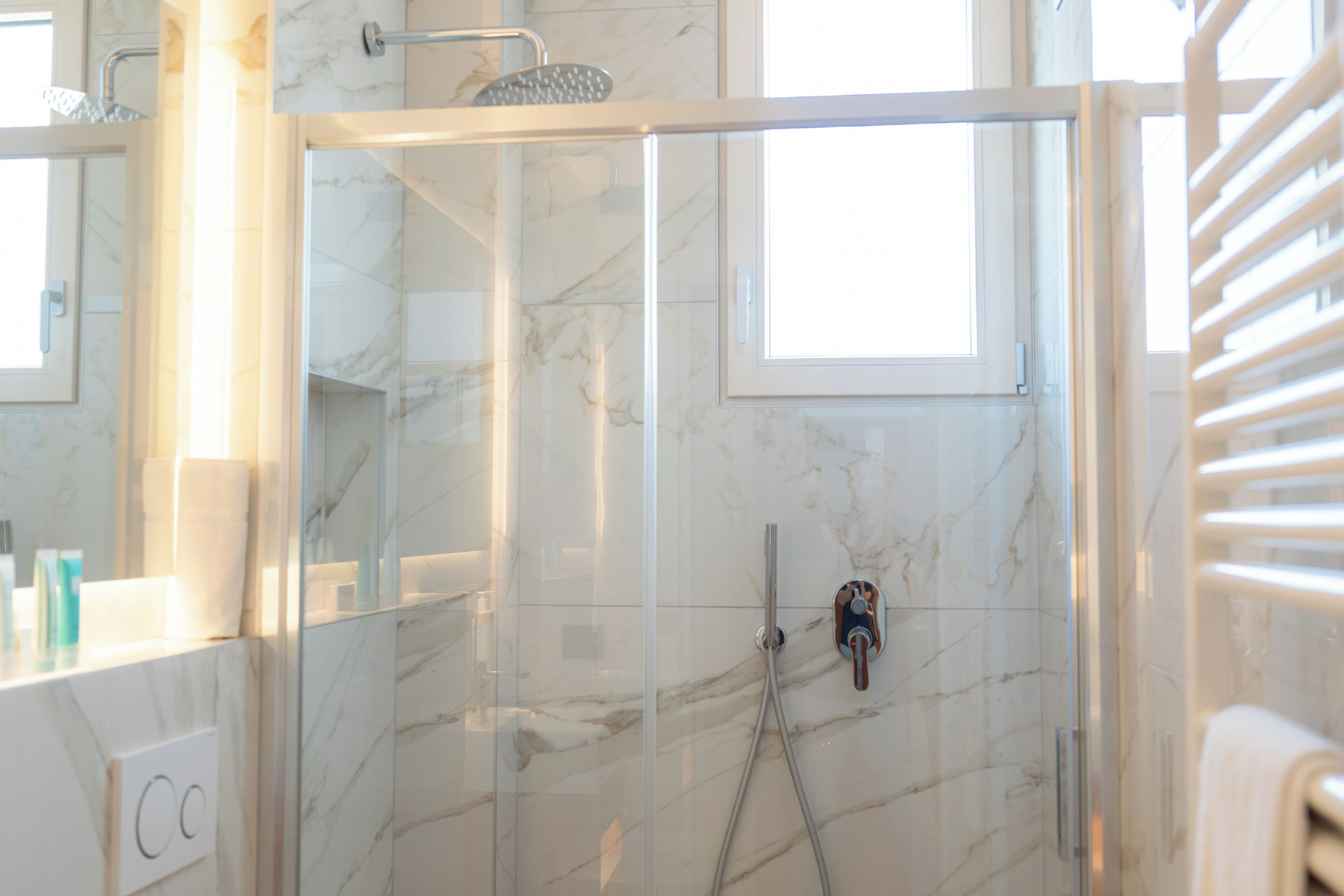 A modern bathroom with a glass-enclosed shower, marble walls, and a visible towel rack.