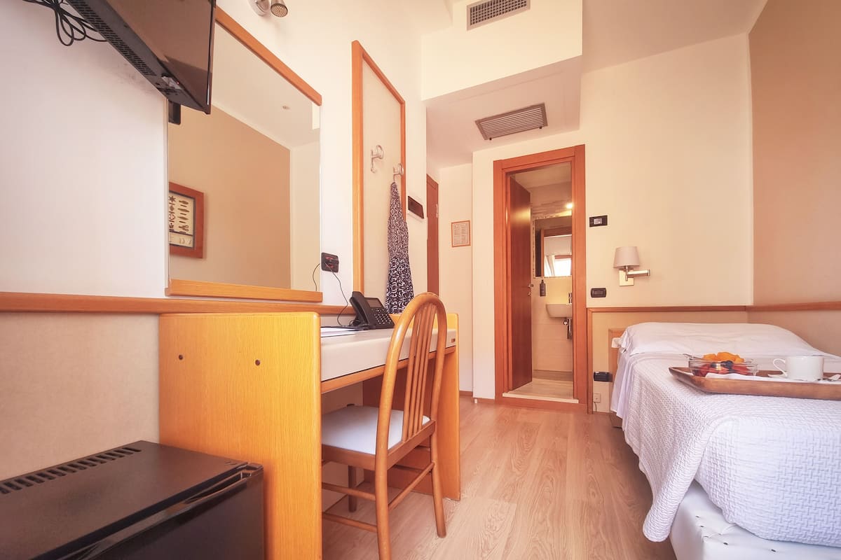 Ett hotellrum med en säng, ett skrivbord med en telefon, en stol, ett litet kylskåp och ett badrum som syns genom en öppen dörr.