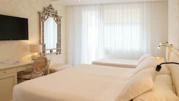 A hotel room with a large bed, a desk with a chair, a television, and a window with sheer curtains.