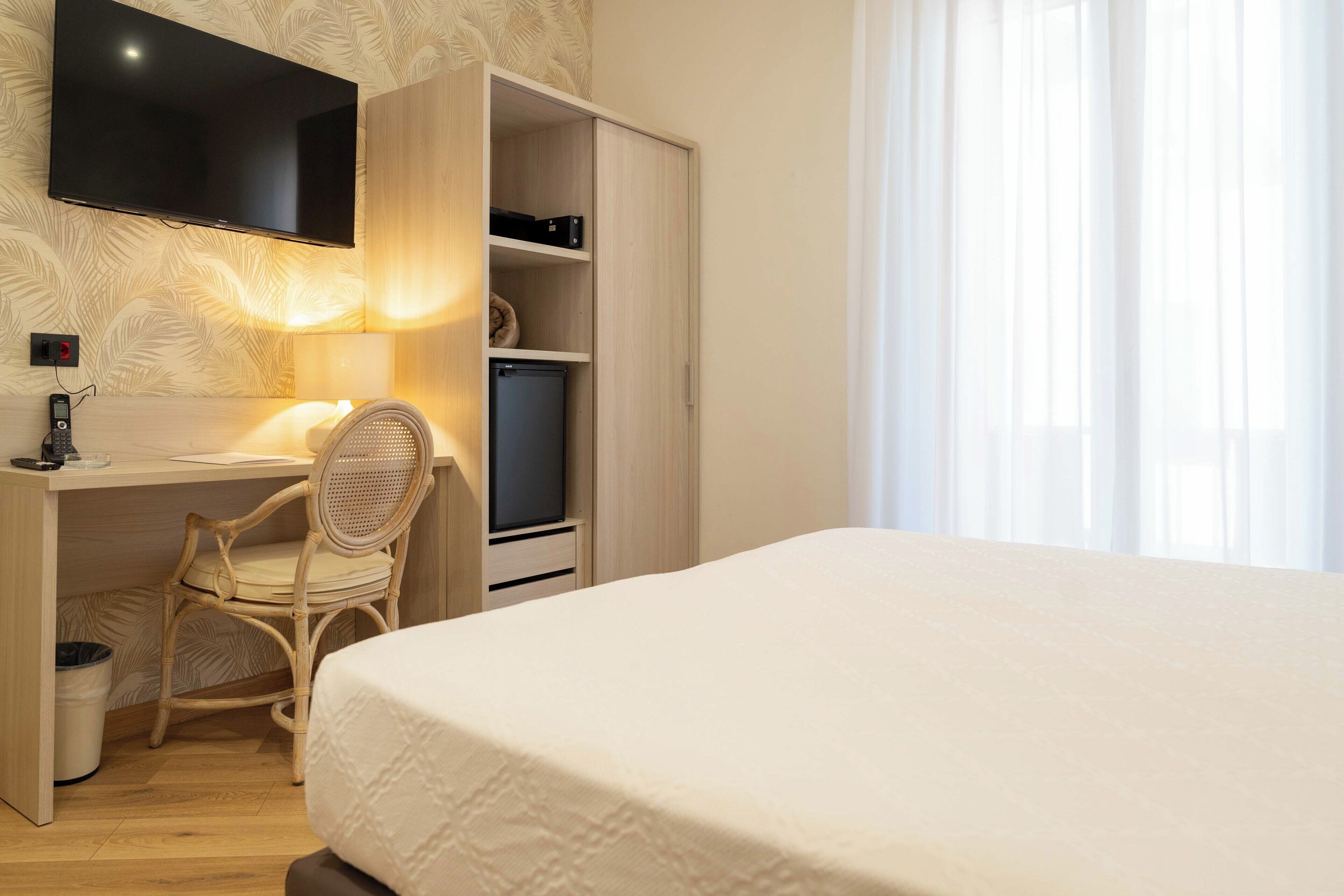 A bedroom with a bed, a desk with a chair, a television, and a wardrobe.