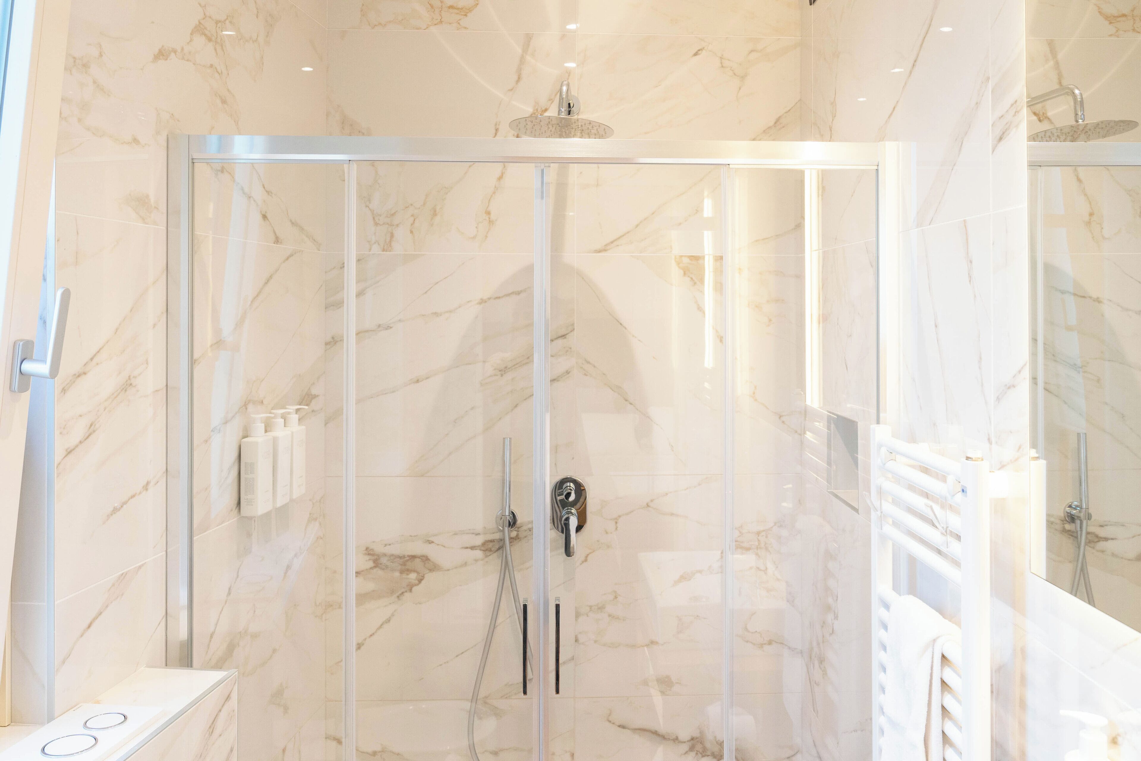 Un bagno moderno con doccia vetrata, pareti in marmo e un piano d'appoggio bianco con porta asciugamani.