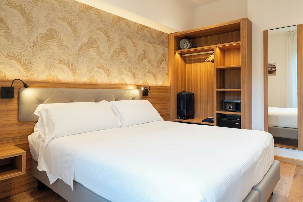 Ett modernt hotellrum med en stor säng, ett träpanelat sänggavel, en inbyggd garderob och en vägg med ett mönster.