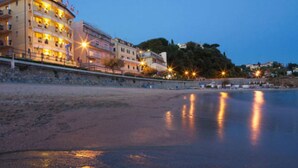 Ein Hotel am Strand mit mehreren Etagen, Balkonen und einer Steinschmalseite.
