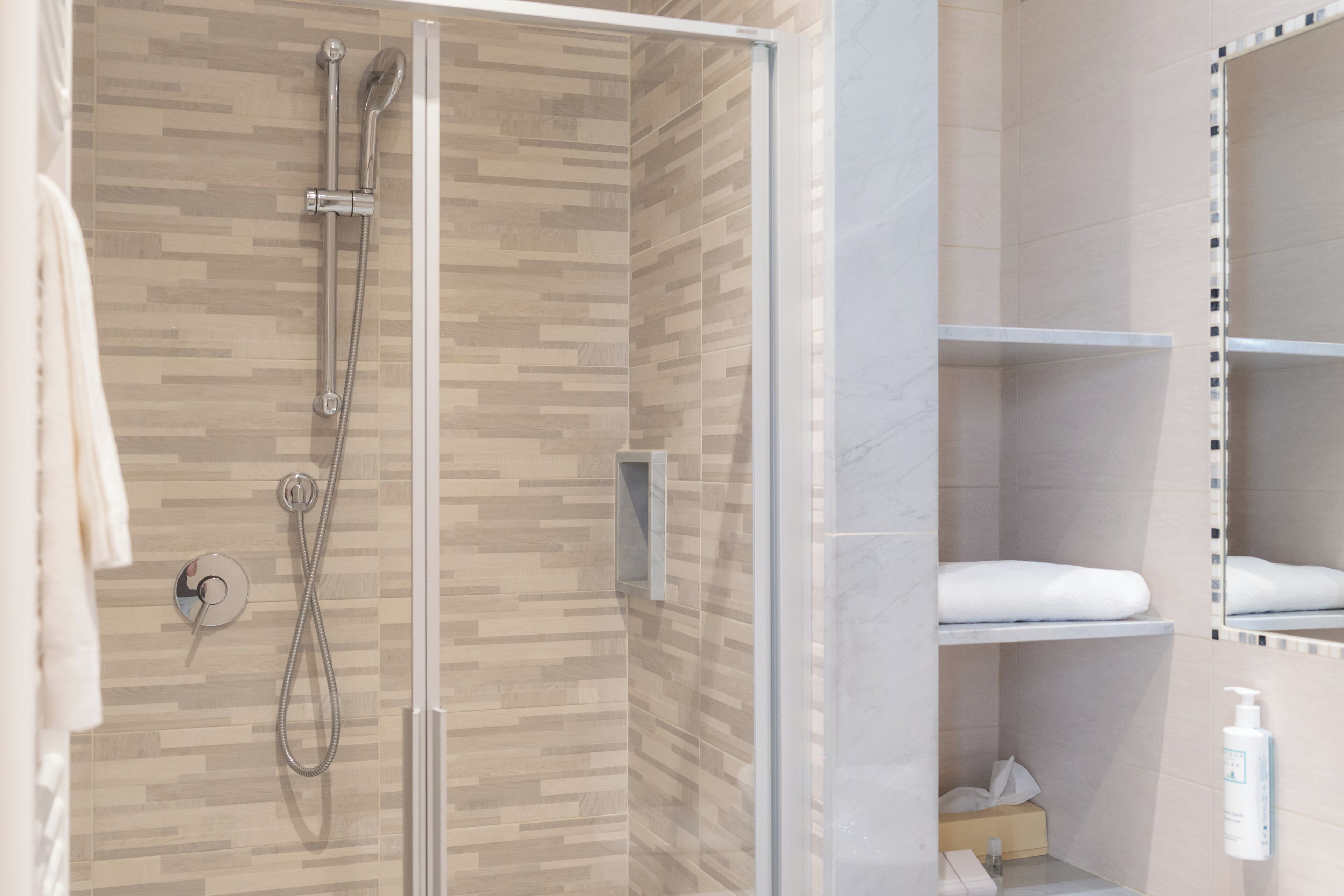 A modern bathroom with a shower enclosure, a towel rack, and a mirror with a decorative frame.