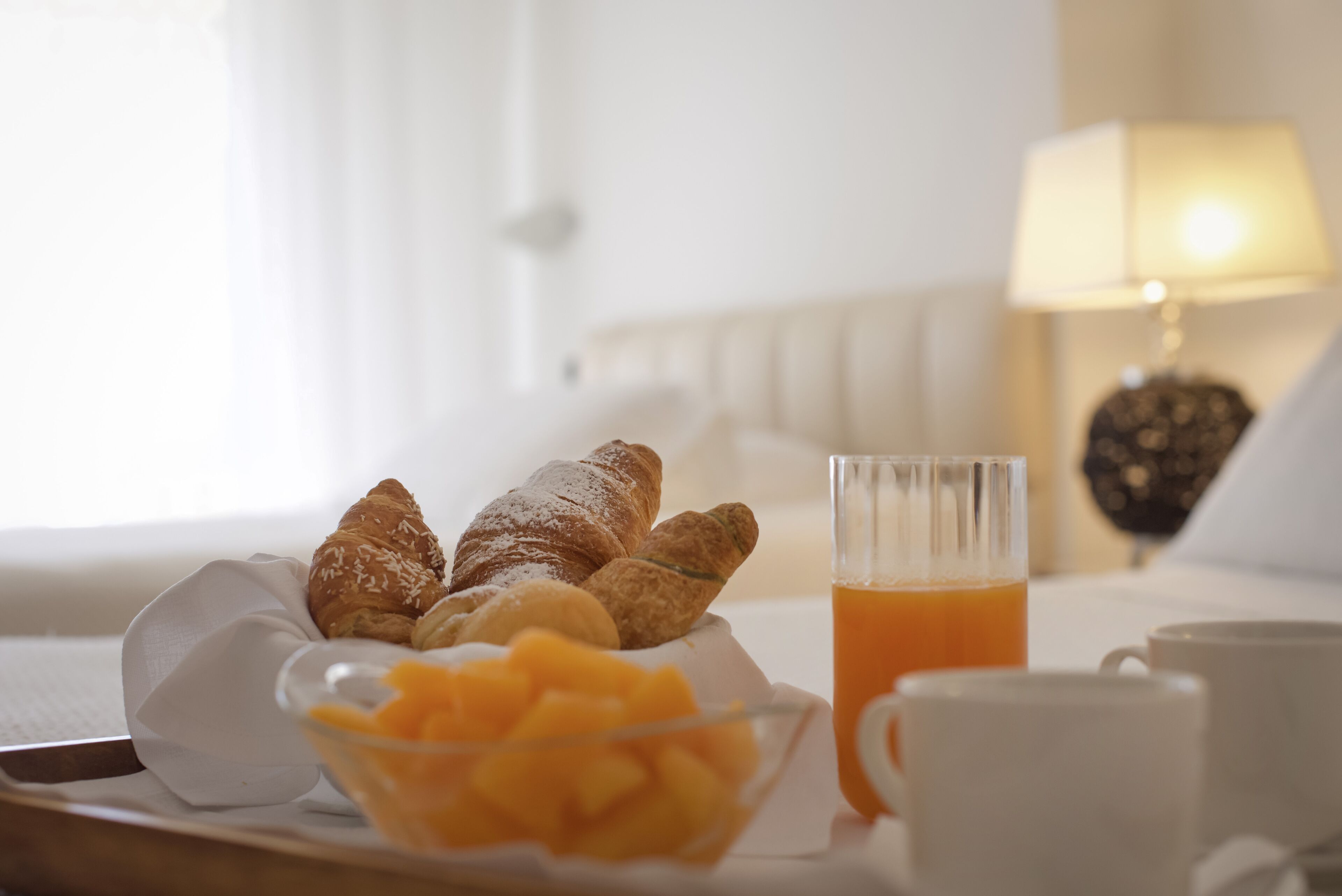Un plateau de petit-déjeuner avec des croissants, du jus d’orange et un bol de fruits, le tout posé sur un lit.
