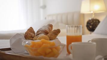 Un plateau de petit-déjeuner avec des croissants, du jus d’orange et un bol de fruits, le tout posé sur un lit.