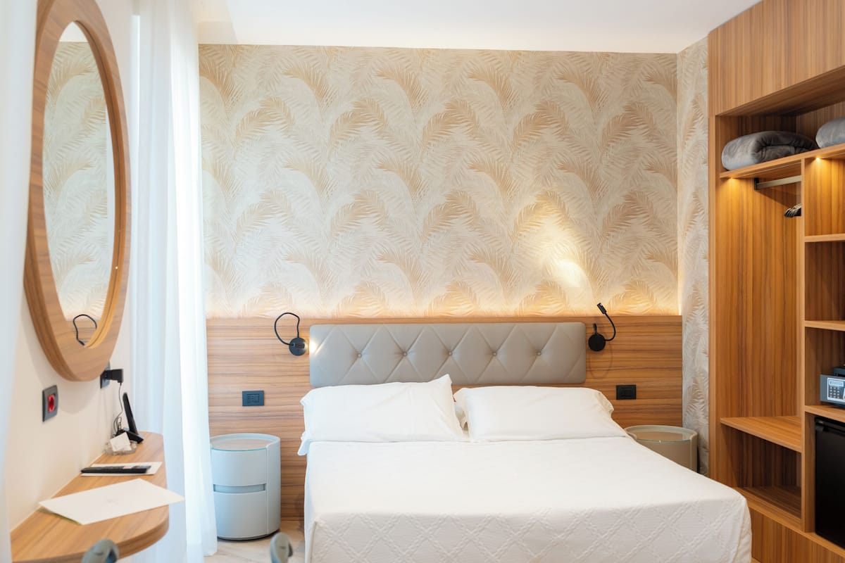 Ett modernt hotellrum med en stor säng, en sänggavel i trä, en inbyggd garderob och en rund spegel.