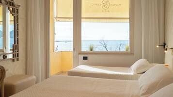 Une chambre d’hôtel avec deux lits, une vue sur la mer et un balcon avec un rideau.