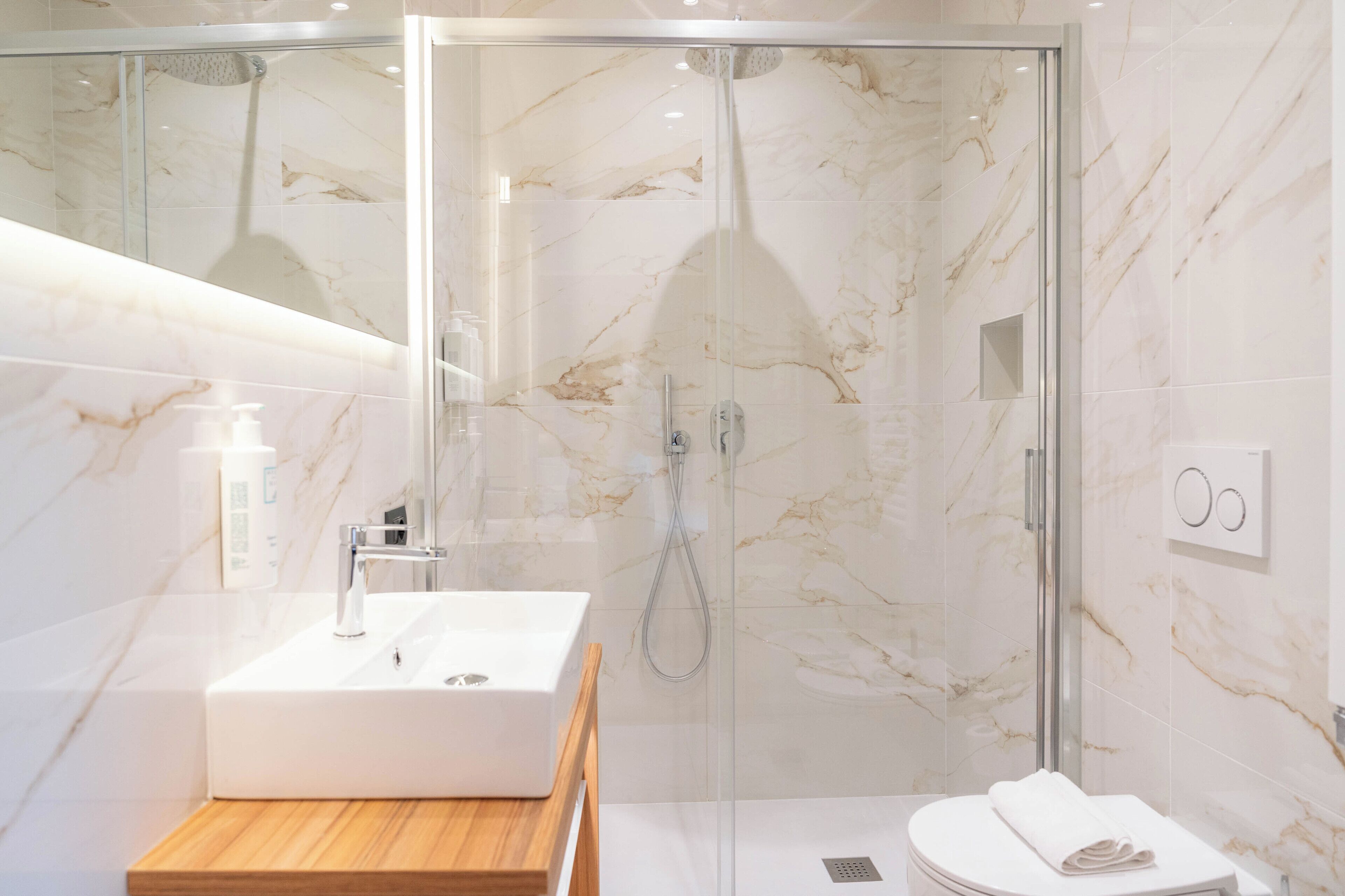 A modern bathroom with a glass-enclosed shower, a white sink with a wooden countertop, and a white toilet.