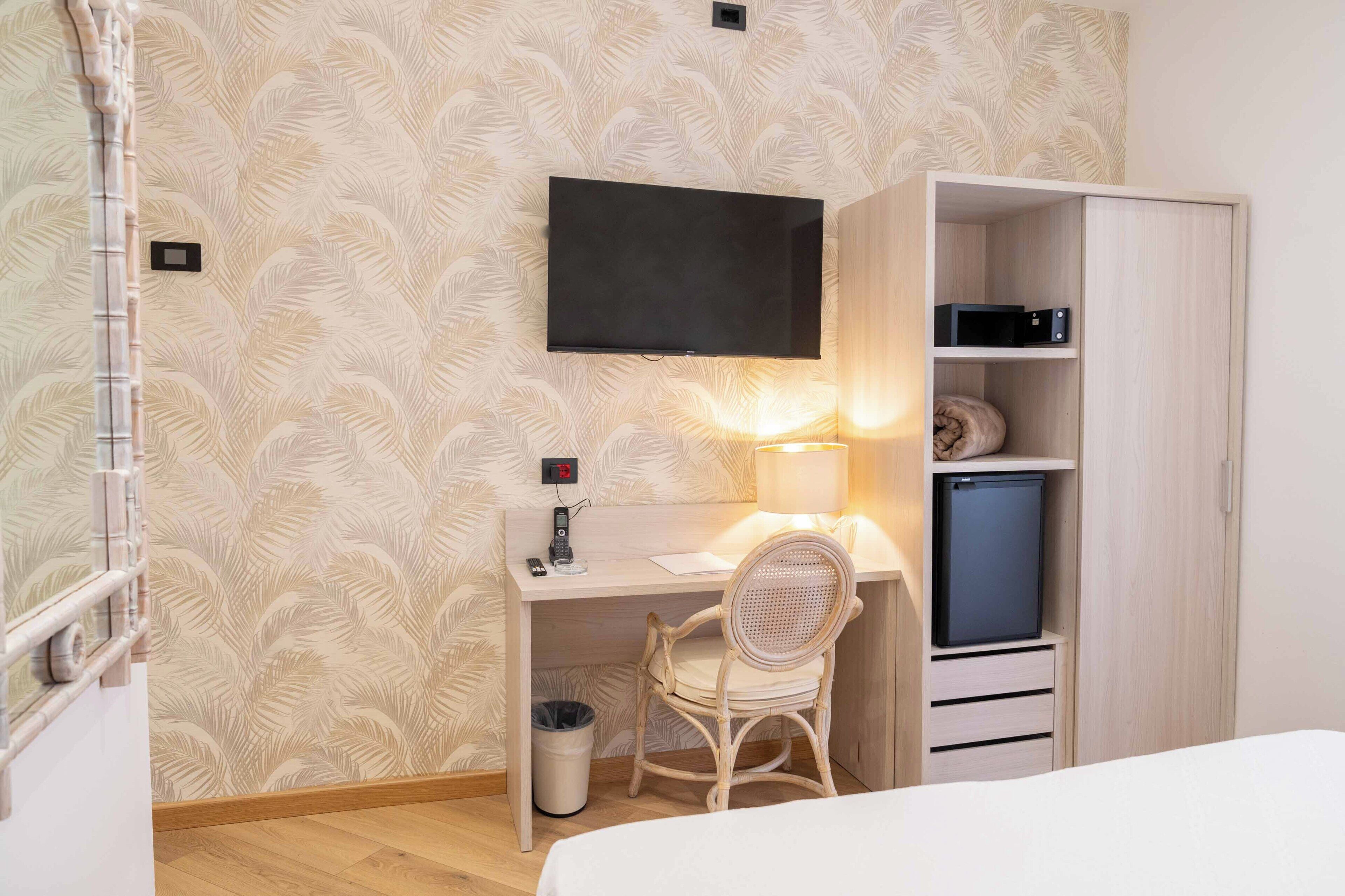 Ein Hotelzimmer mit Bett, Schreibtisch mit Stuhl, Wandfernseher, Kleiderschrank und kleinem Kühlschrank.