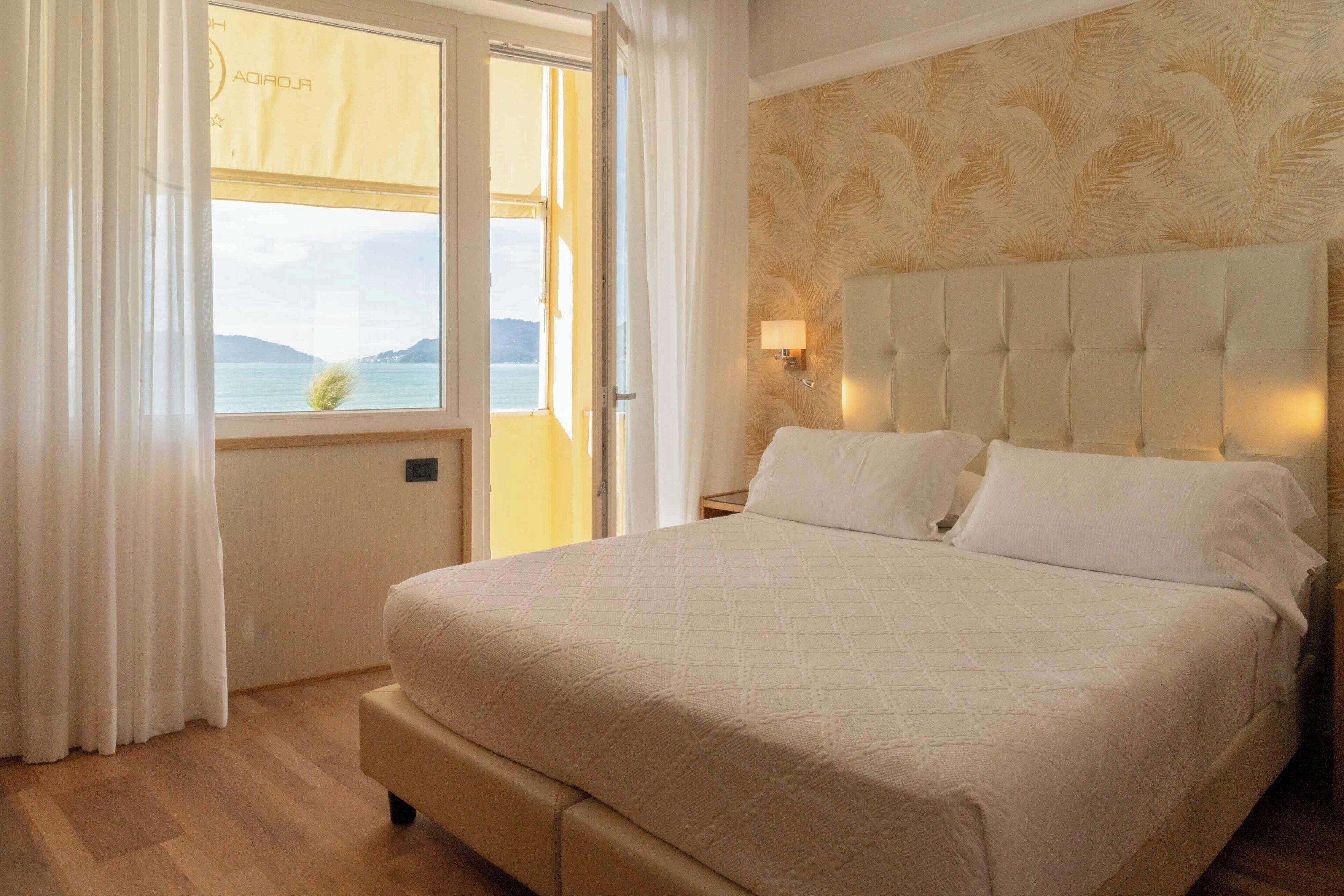 A bedroom with a large bed, a window with curtains, a headboard with a light, and a patterned wall.