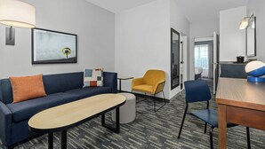 Una habitación de hotel moderna con sofá, sillón, reposapiés y una mesa de comedor.