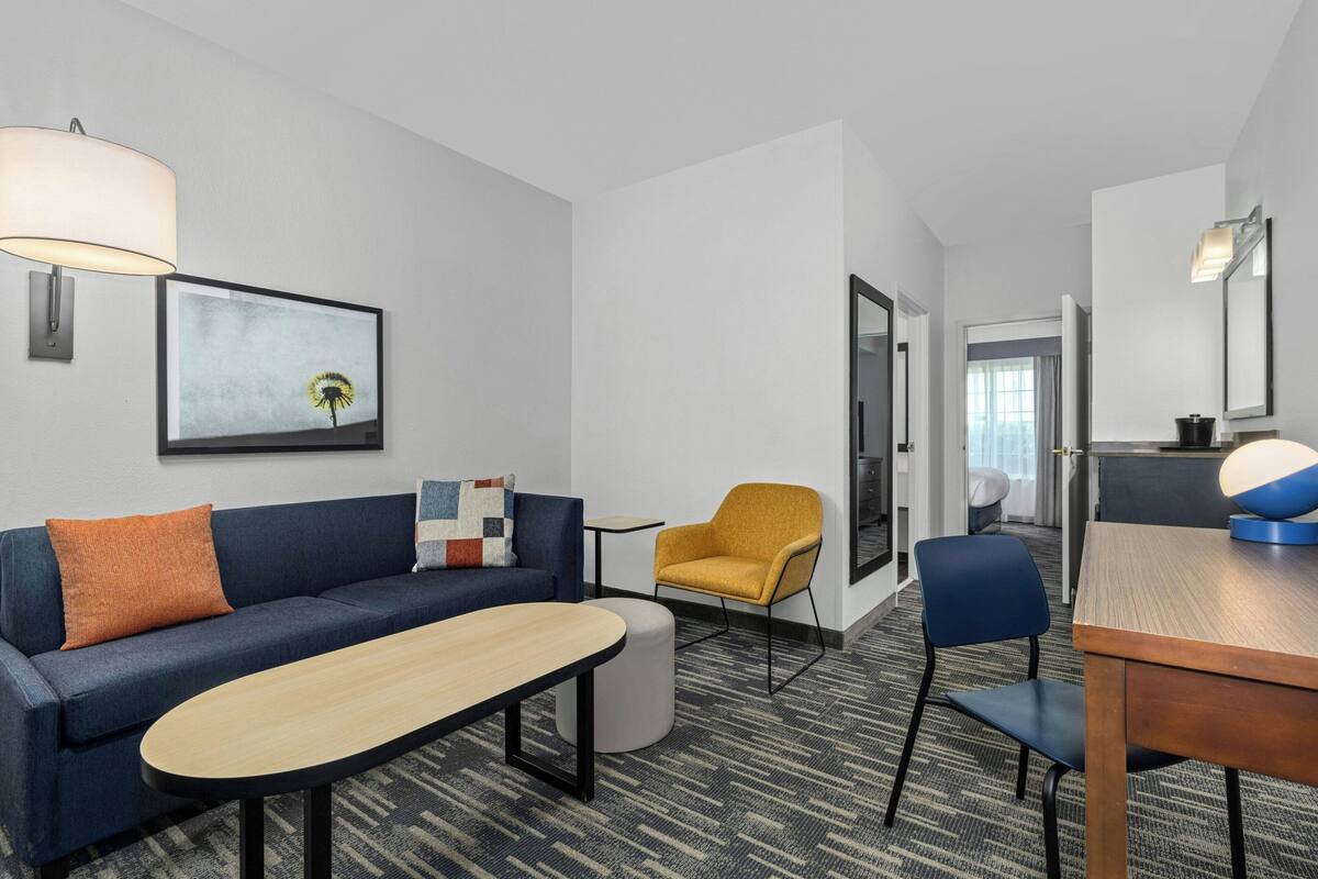 A modern hotel room with a sofa, armchair, ottoman, and a dining table.