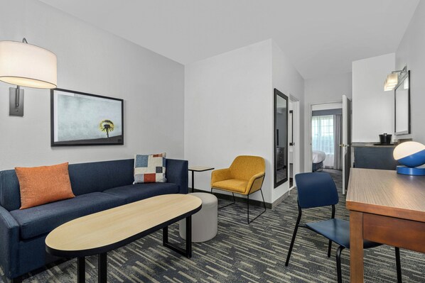 Quarto de hotel moderno com sofá, poltrona, banquinho e mesa de jantar.
