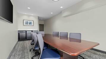 A conference room with a long table, six chairs, a projector screen, and a framed picture on the wall.