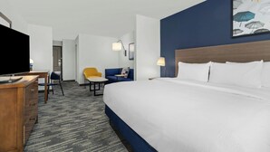 Habitación de hotel con cama, escritorio, silla, televisor y un cuadro en la pared.