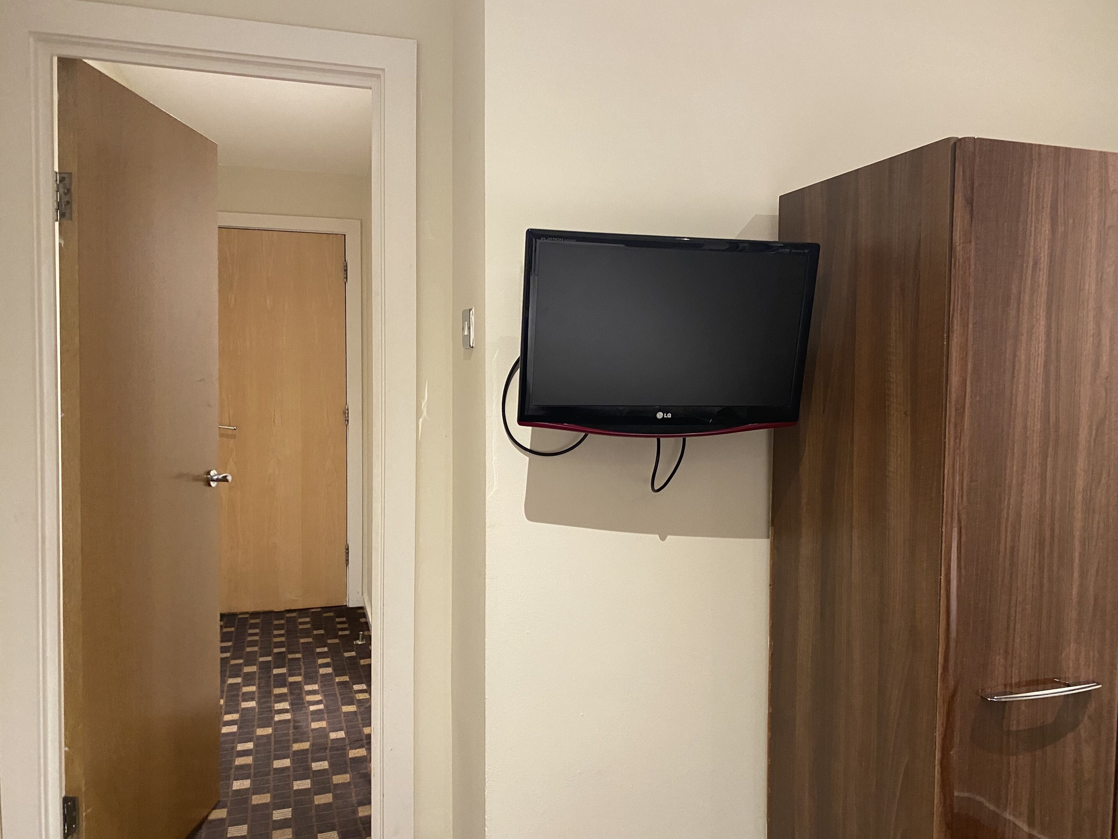 Een kamer met een houten garderobe, een aan de muur bevestigde televisie en een kamer met een patroon vloer.