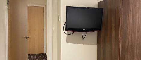 A room with a wooden wardrobe, a television mounted on the wall, and a patterned floor.